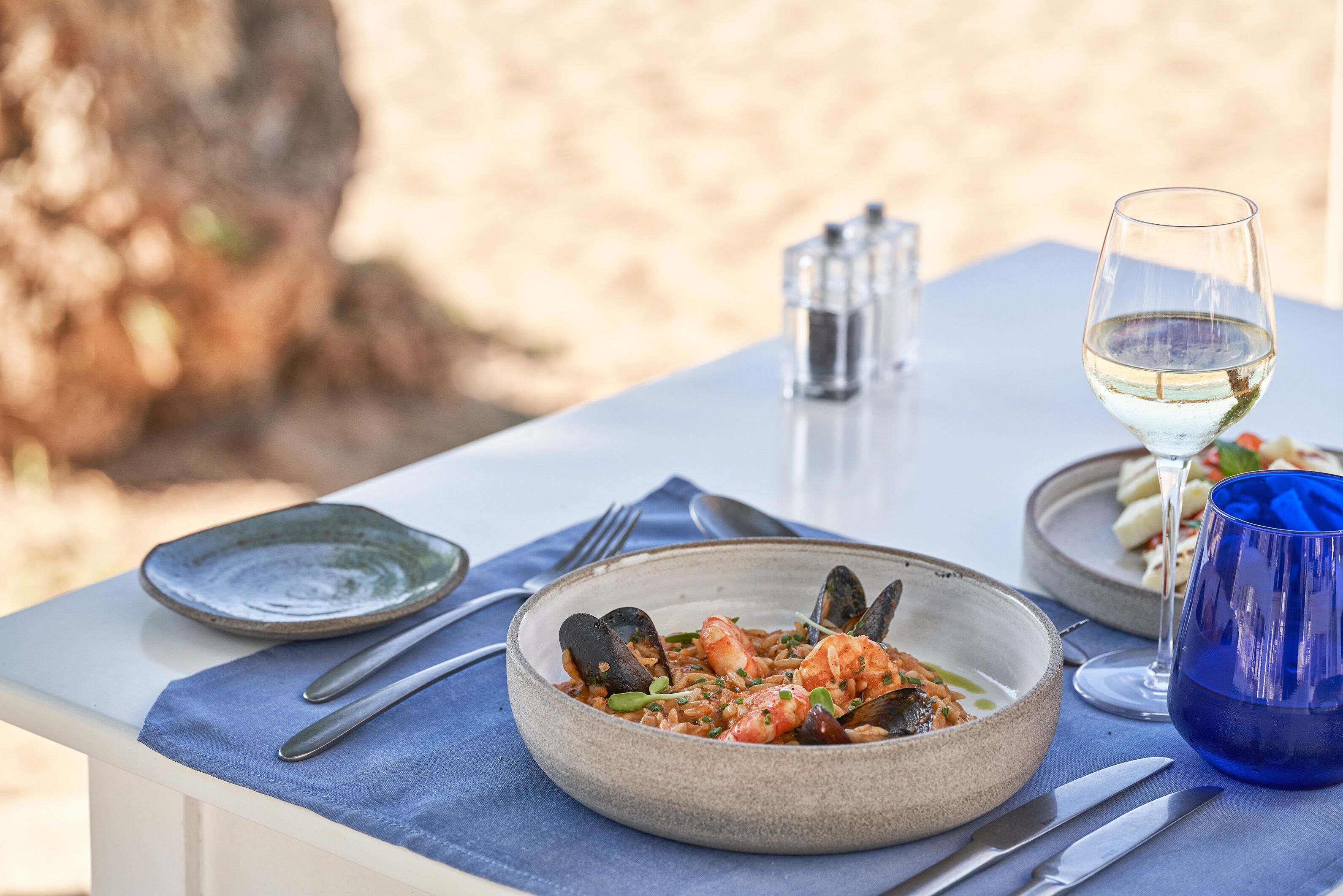 A dining table with a seafood dish, a glass of white wine, and a blue cup.
