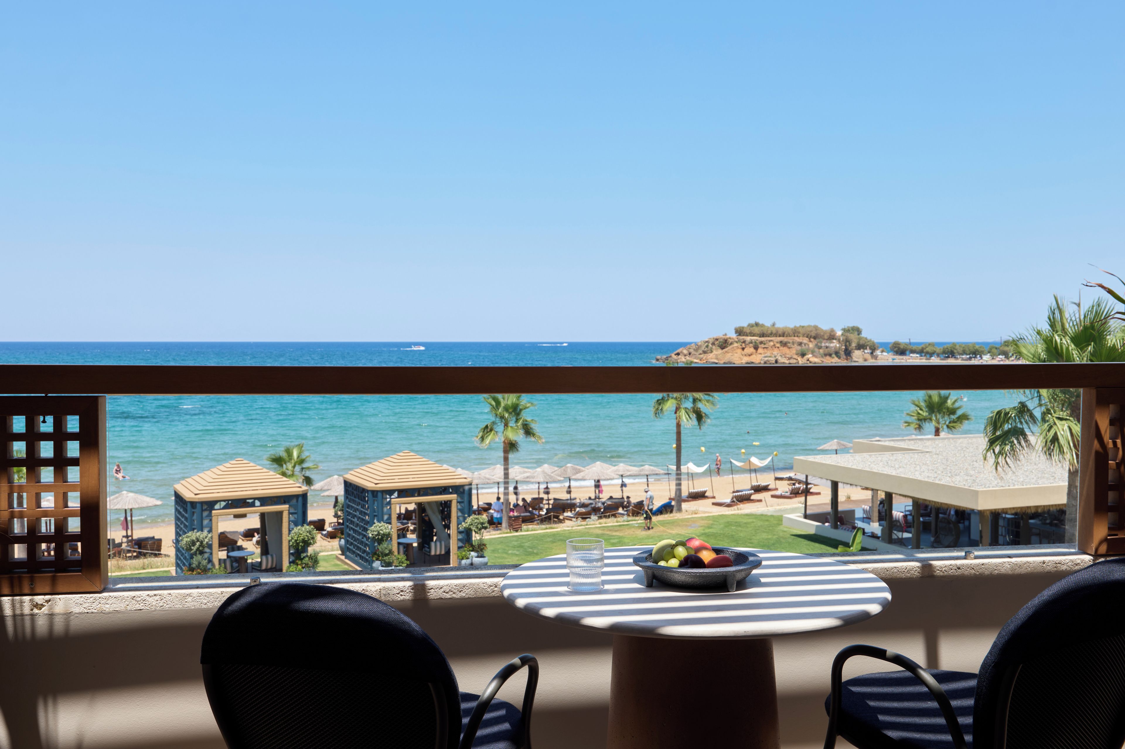 A balcony with a view of the sea, a table with a fruit bowl, and outdoor seating.