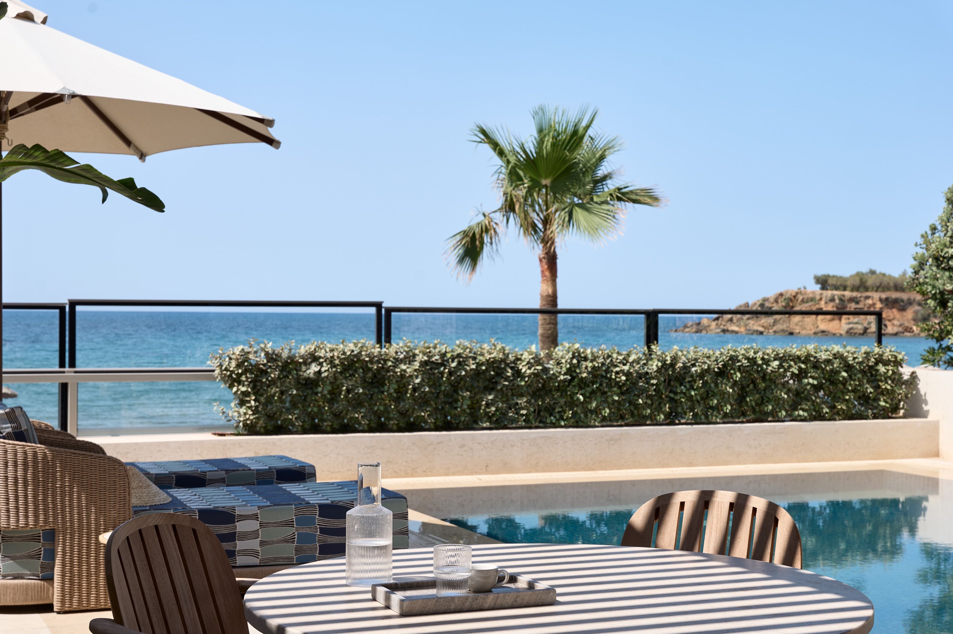 Zona de piscina con vista al mar, una palmera y un promontorio rocoso.