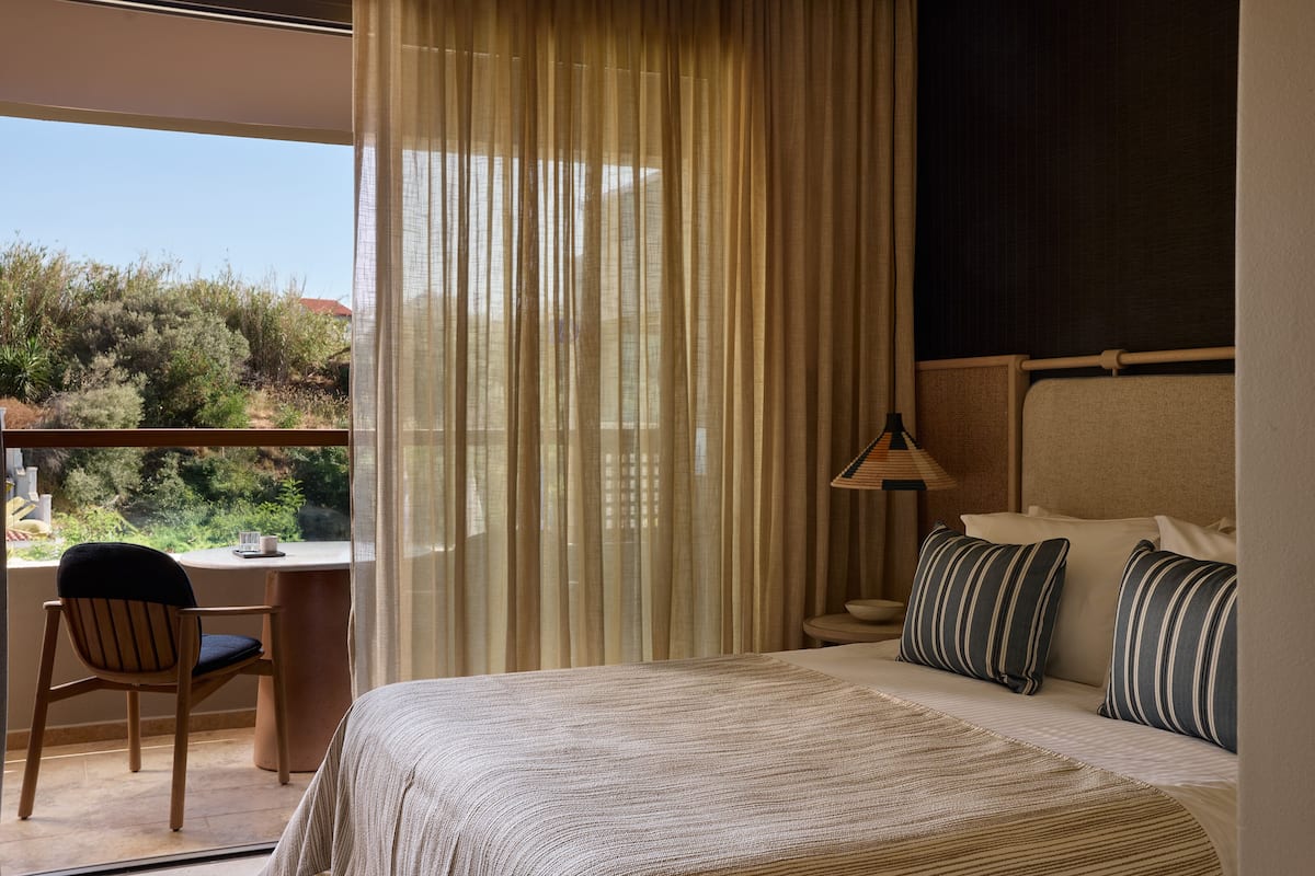 Habitación de hotel con cama, escritorio y silla. Cuenta con una ventana con cortinas y vistas al exterior.