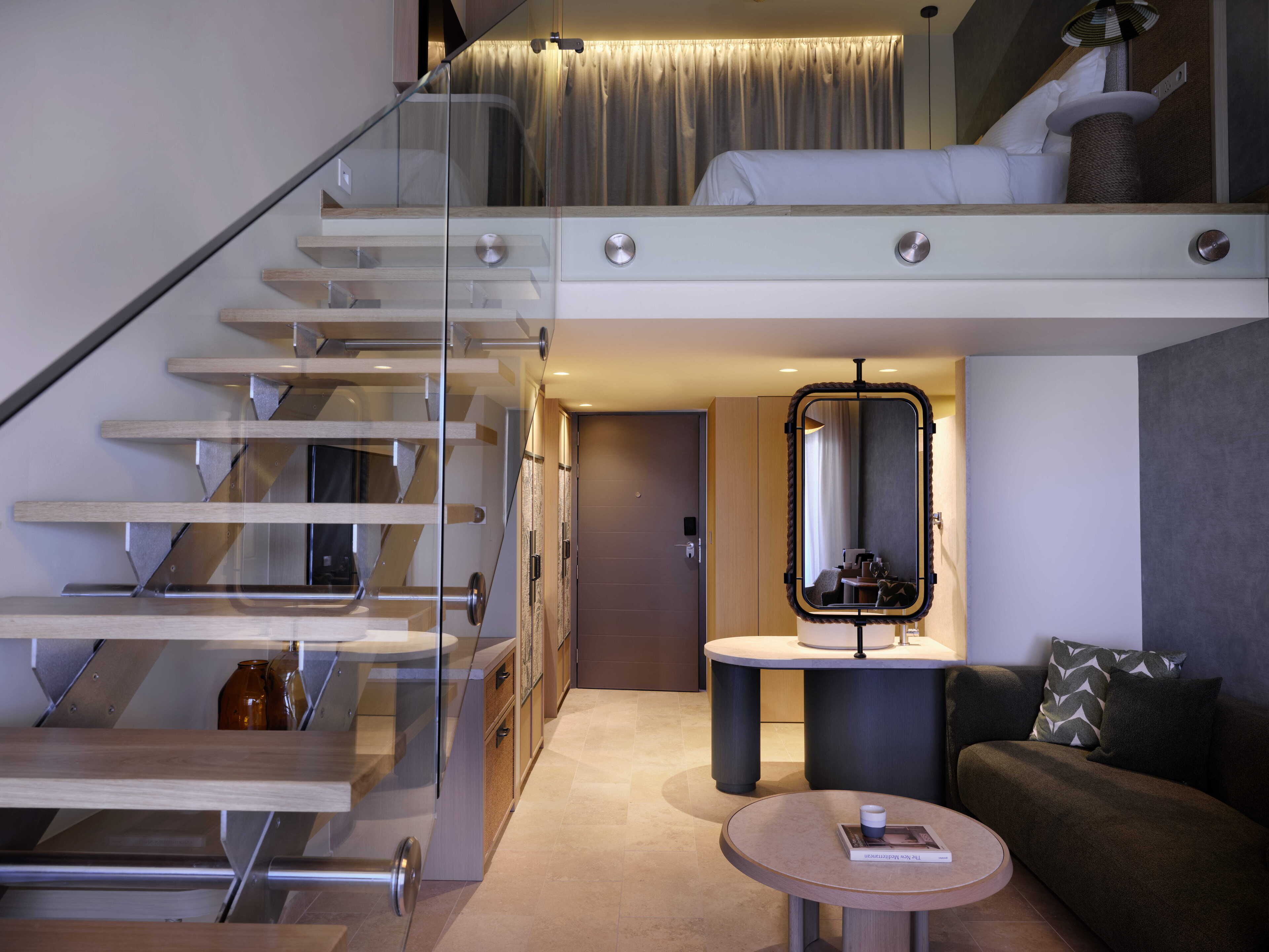 A modern interior with a glass staircase, a round coffee table, a sofa, and a mirror.