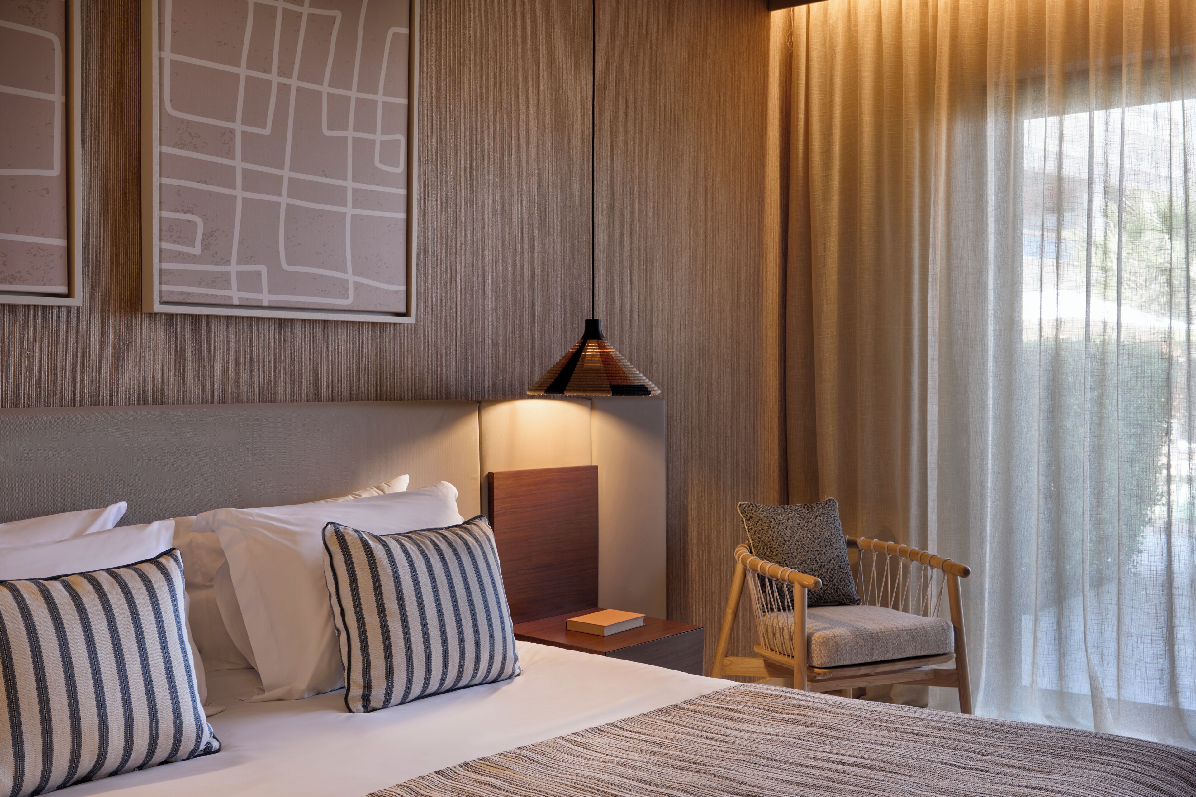 A hotel room with a bed, a chair, a map on the wall, and a lamp.