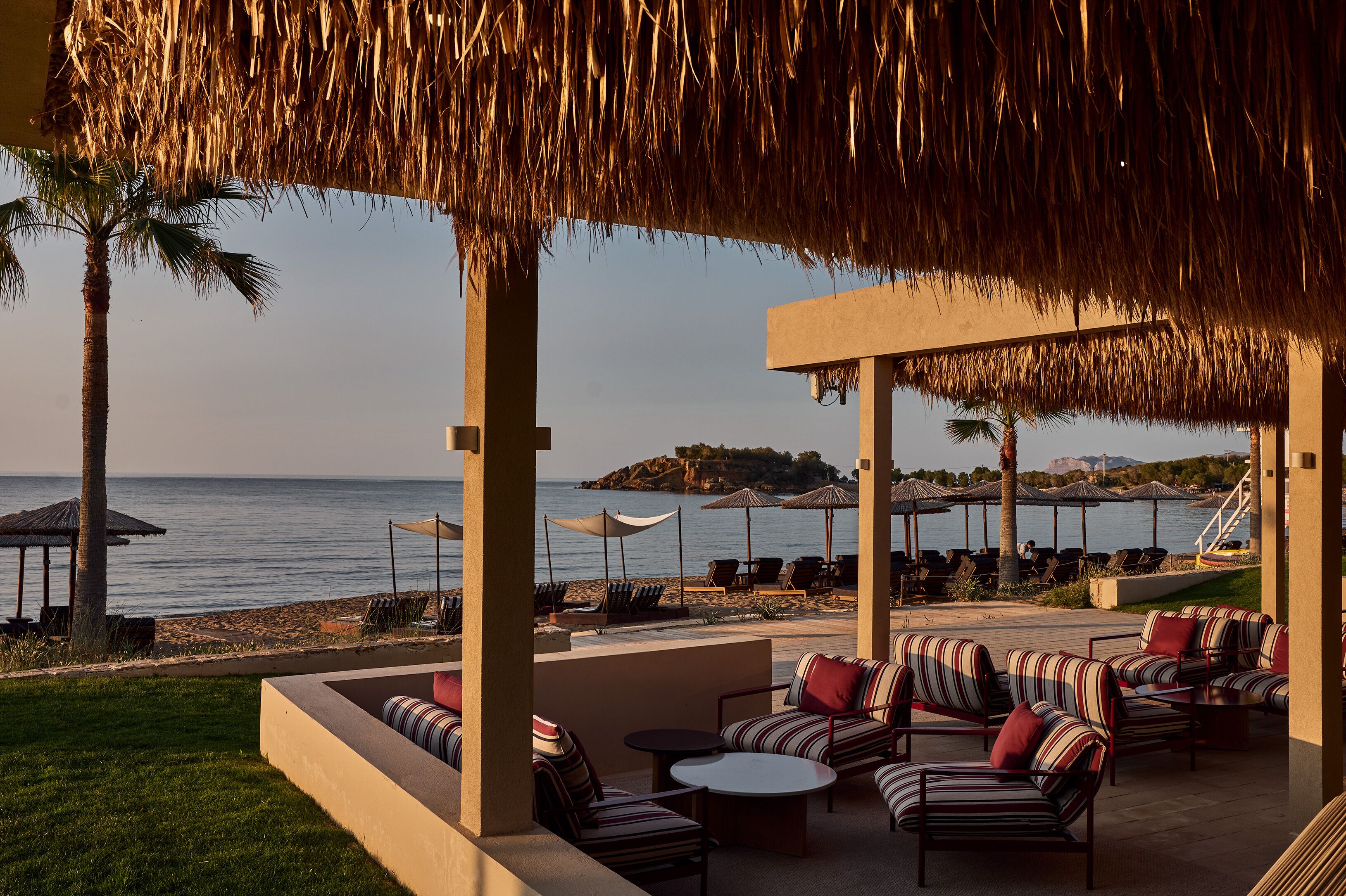 A beachside patio with striped sofas, umbrellas, and a view of the sea.