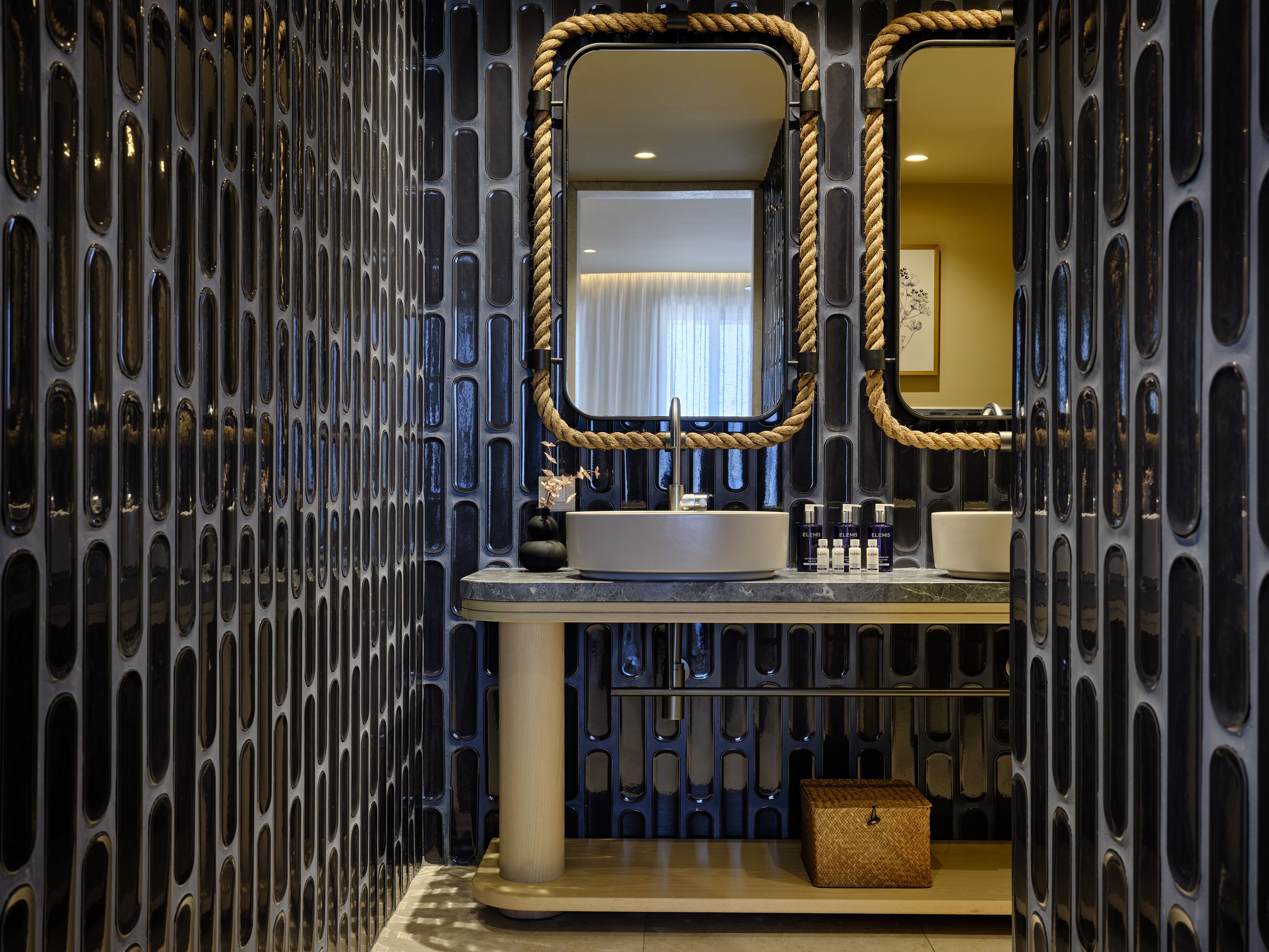 Une salle de bain au design moderne, dotée d’un grand miroir, d’un lavabo et d’une corde décorative.