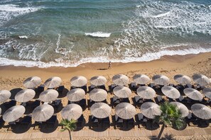 Une plage bordée de rangées de chaises longues et d’ombrelles en chaume, une plage de sable fin, et l’océan avec ses vagues.