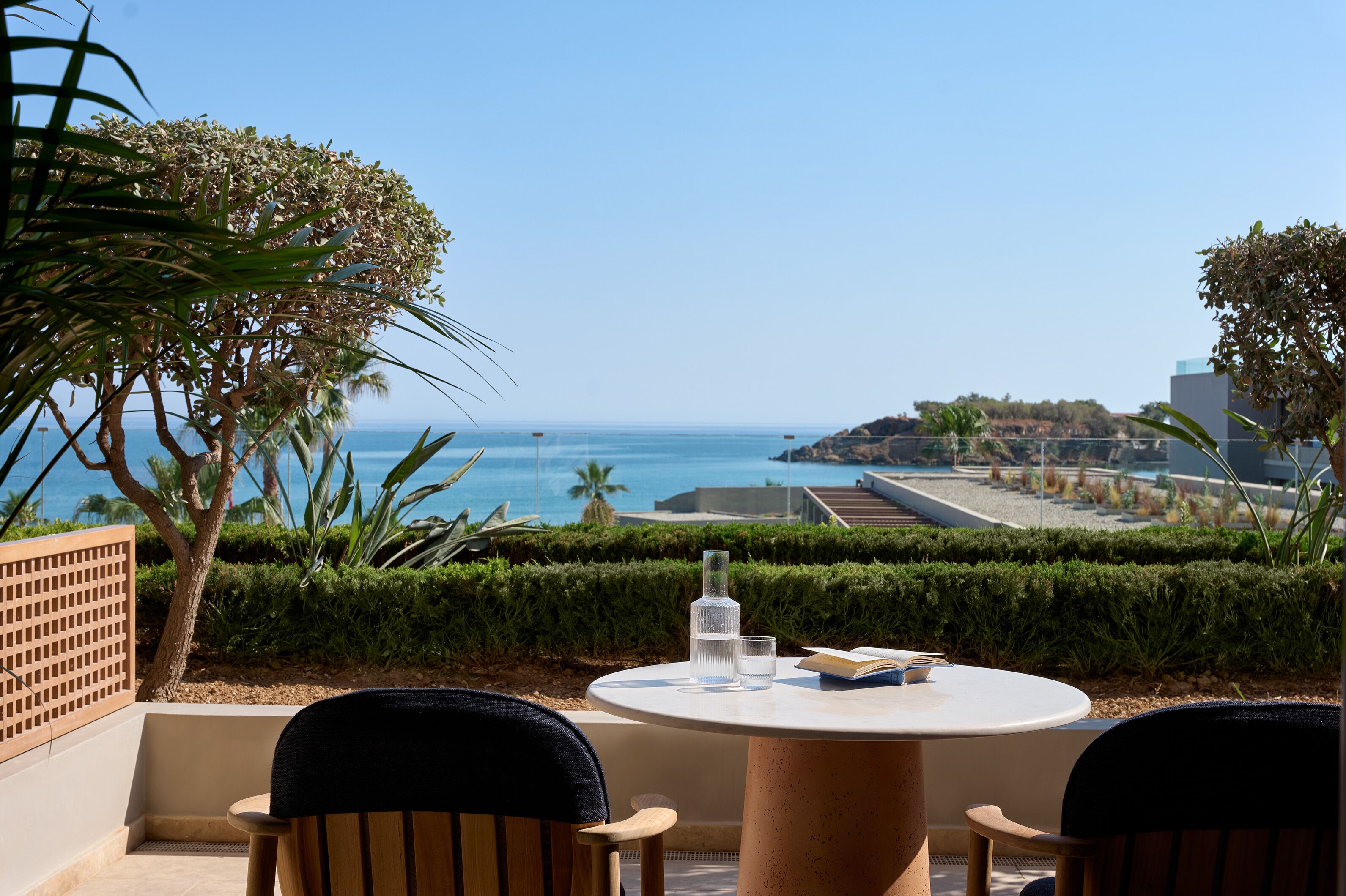 A round table with chairs, a bottle, and glasses on a terrace overlooking the sea.