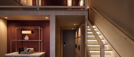 A multi-level interior with a staircase, a hallway leading to a door, and a counter with items on it.
