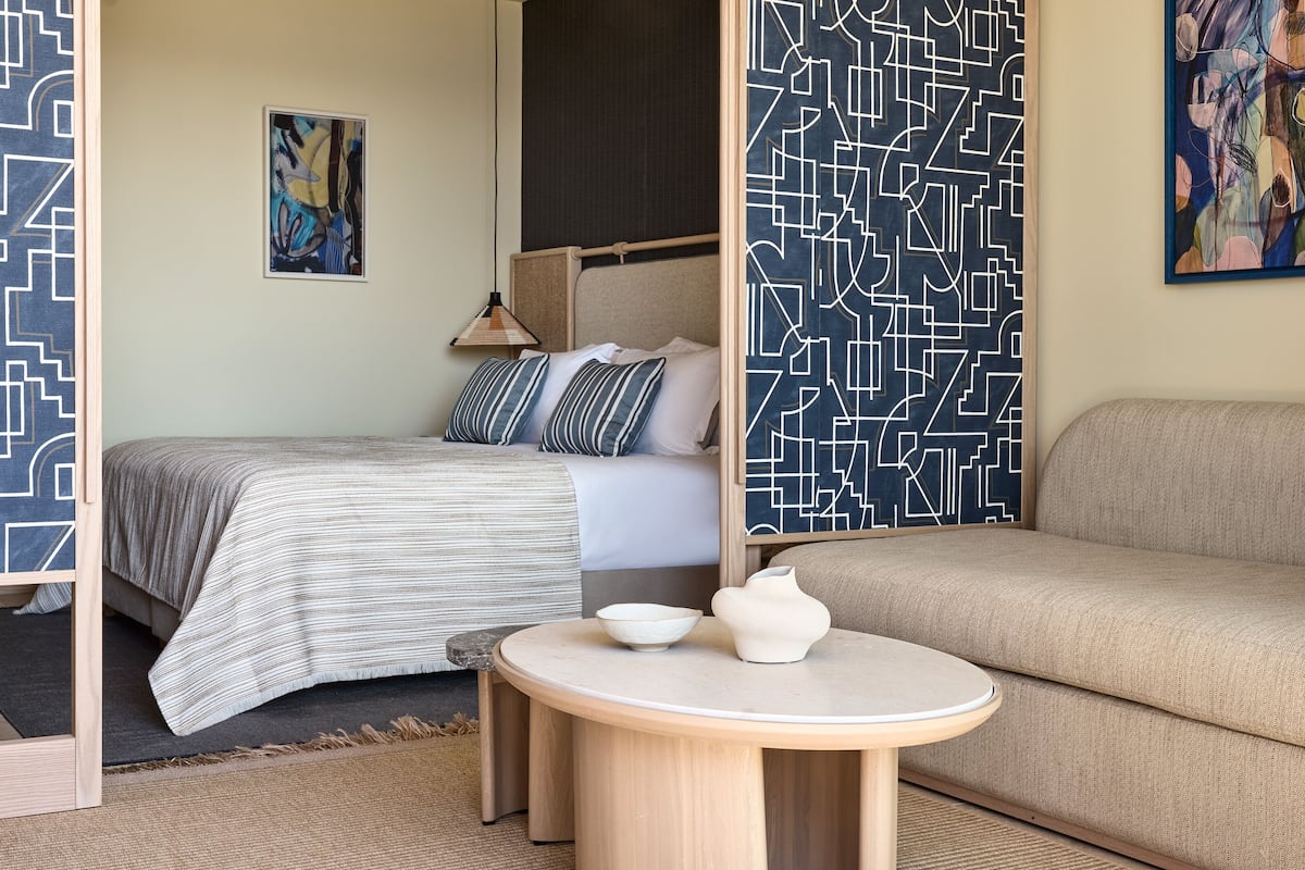 Un dormitorio con una cama, un sofá, una mesa redonda con un cuenco y un jarrón, y arte abstracto en las paredes.