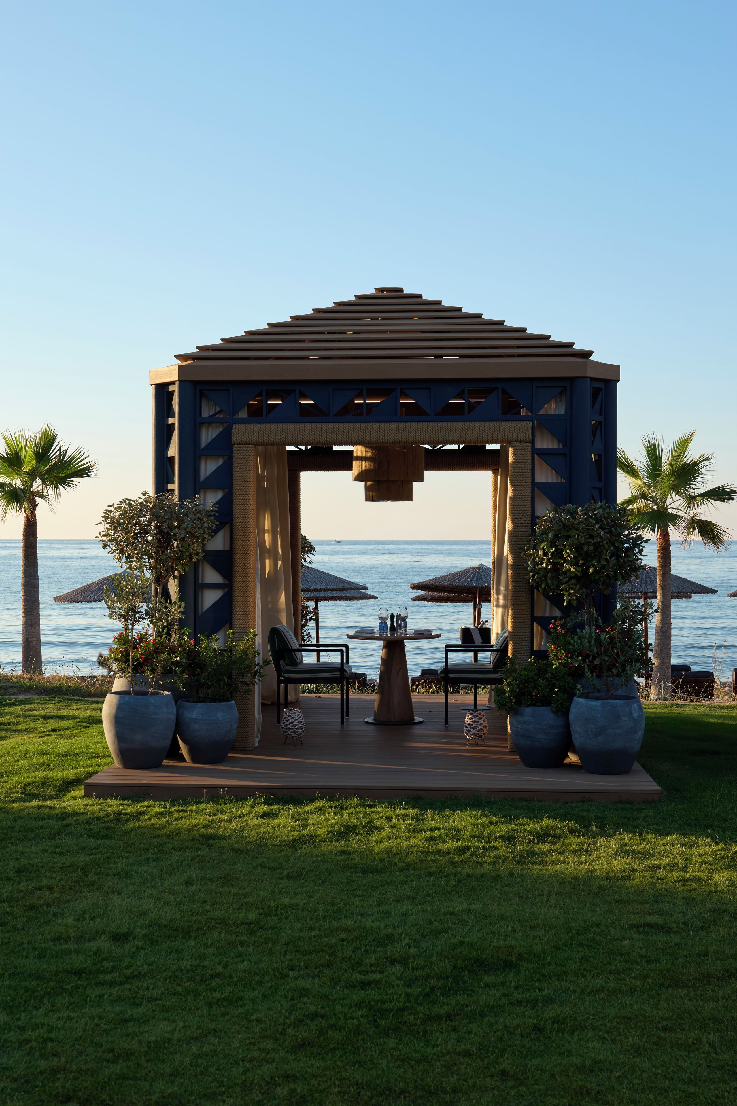 A gazebo with a view of the sea, outdoor seating, and potted plants.