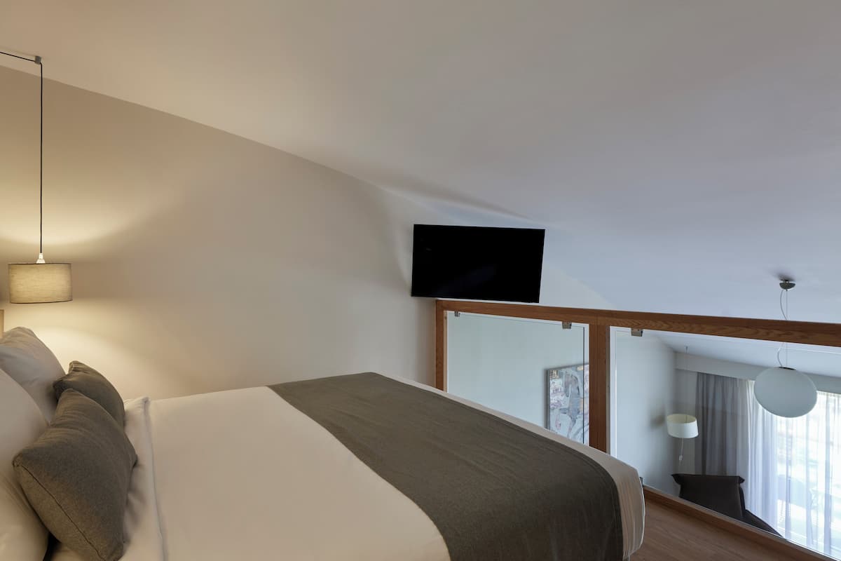 Una habitación de hotel moderna con una cama grande, un televisor de pantalla plana montado en la pared y un balcón con vistas.