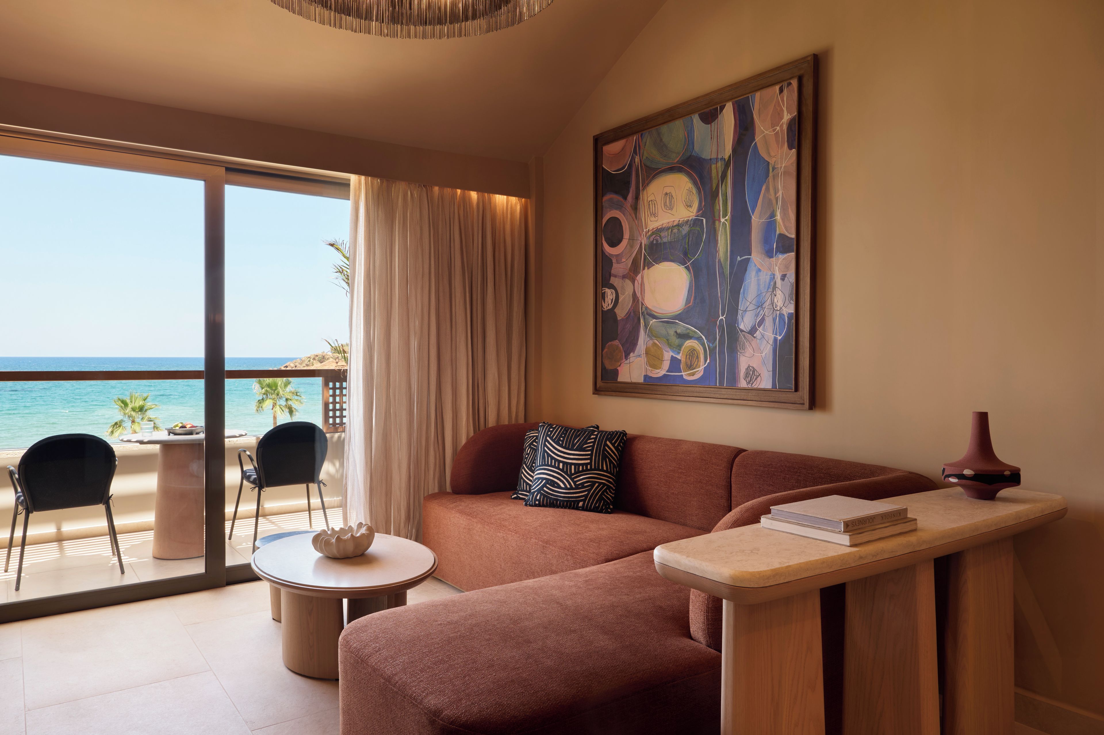A modern living room with a sofa, a small round table, and a view of the ocean through large glass doors.