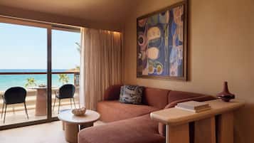 A modern living room with a sofa, a small round table, and a view of the ocean through large glass doors.