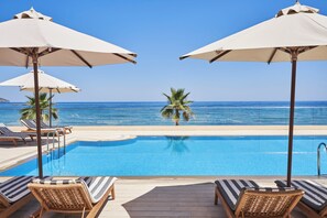 Un espace aménagé au bord de la piscine, avec des chaises longues et des parasols, offrant une vue sur une mer d’un bleu limpide.