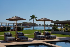 Un espace aménagé au bord de la piscine, avec des chaises longues et des parasols, offrant une vue sur une étendue d’eau et une côte rocheuse.