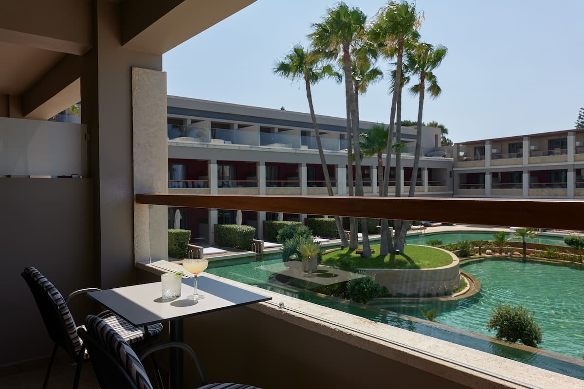 Un balcón con mesa y sillas, con vista a una piscina y un edificio con varios balcones.