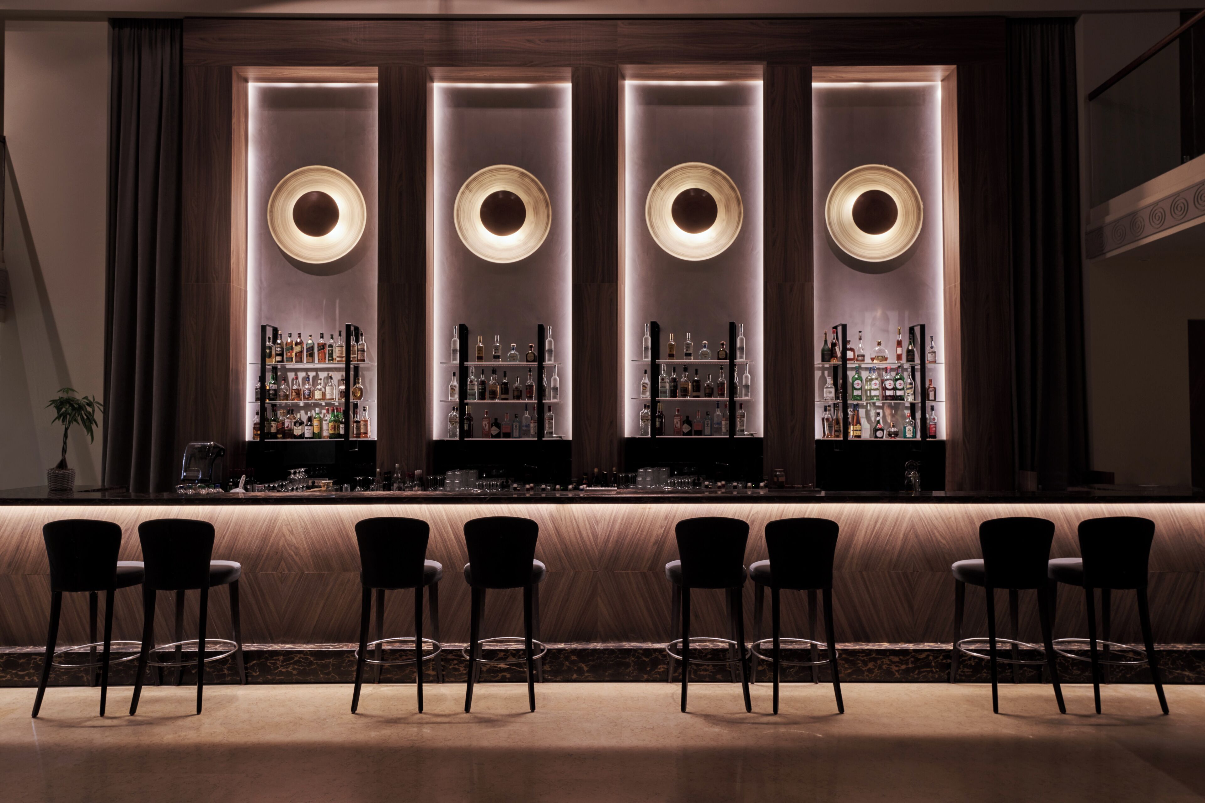 A bar area with a counter, bar stools, and shelves of bottles.
