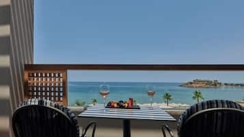 A table with two chairs and a fruit platter, two wine glasses, and a view of the sea and a small island.