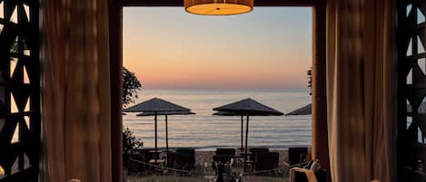 A dining area with a table and chairs, a hanging light fixture, and a view of the sea.