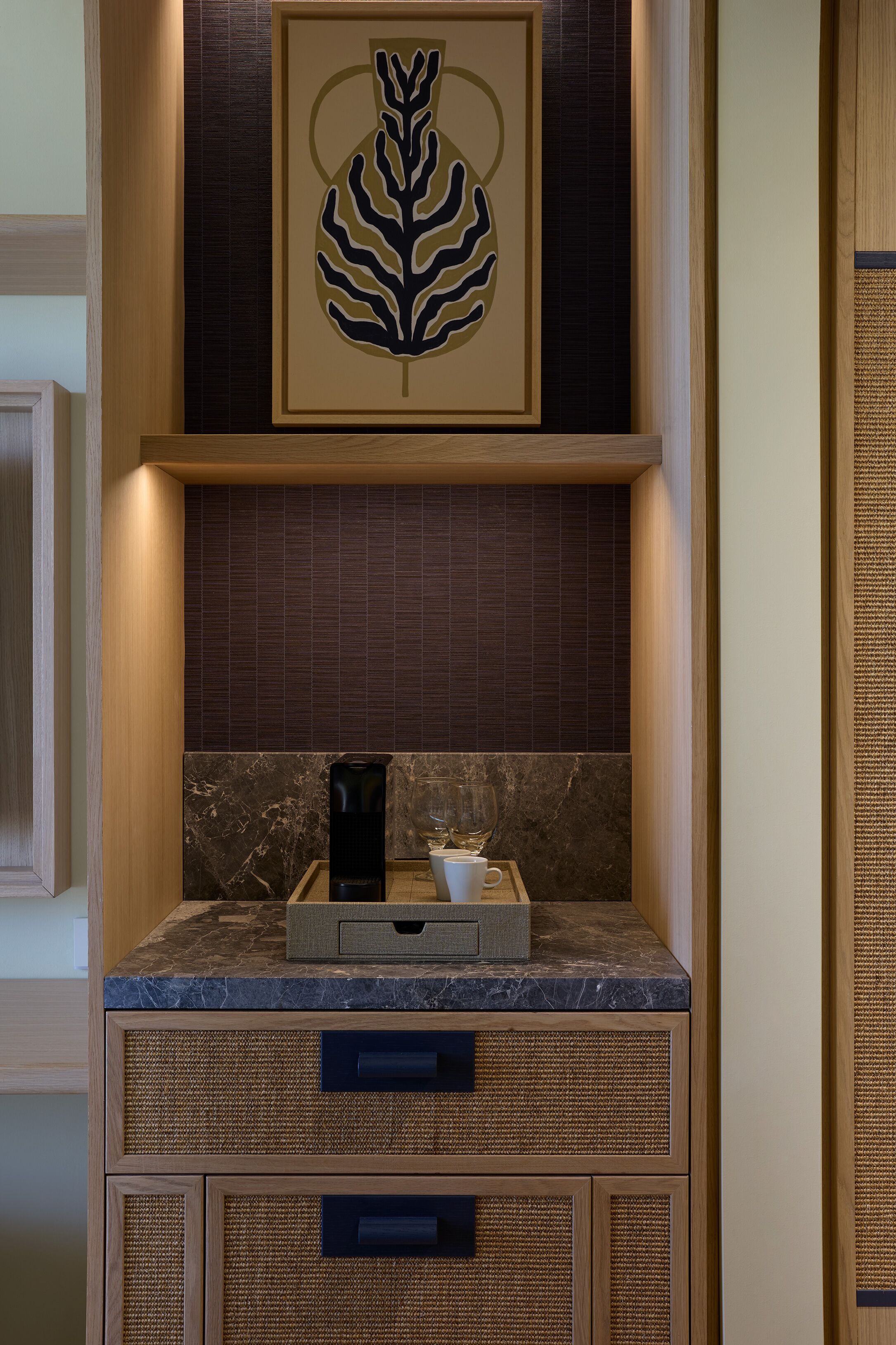 A modern kitchen with a marble countertop, a coffee machine, and a framed artwork above the counter.