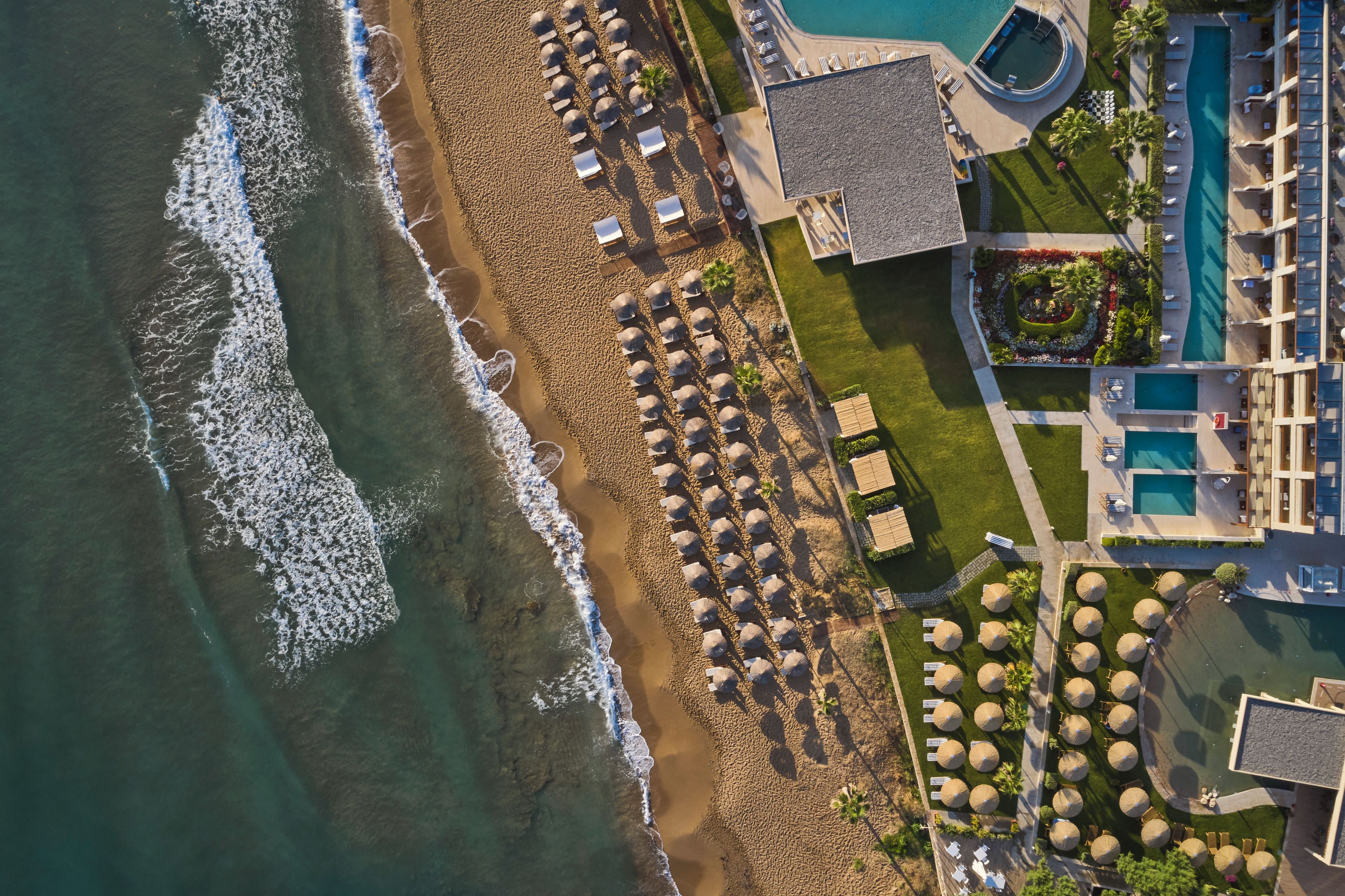 An aerial view of a beach resort with a pool, umbrellas, and lounge chairs.
