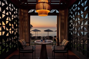 Un espace de restauration en plein air offrant une vue sur la mer, comprenant une table avec des chaises, un luminaire suspendu et un mur en treillis de bois.
