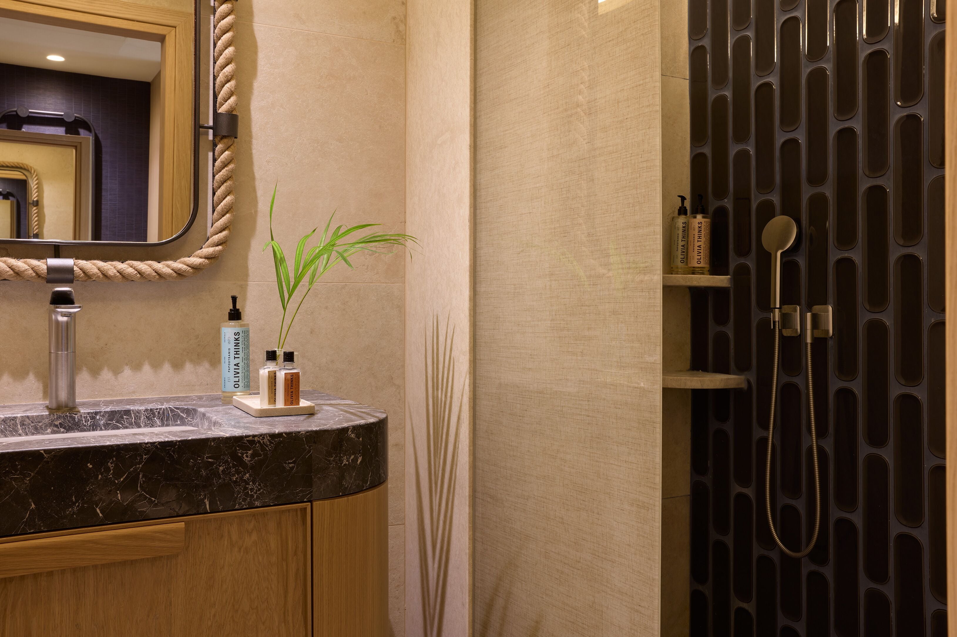 A bathroom with a marble sink, a mirror with a rope frame, a potted plant, and a shower with a black panel design.