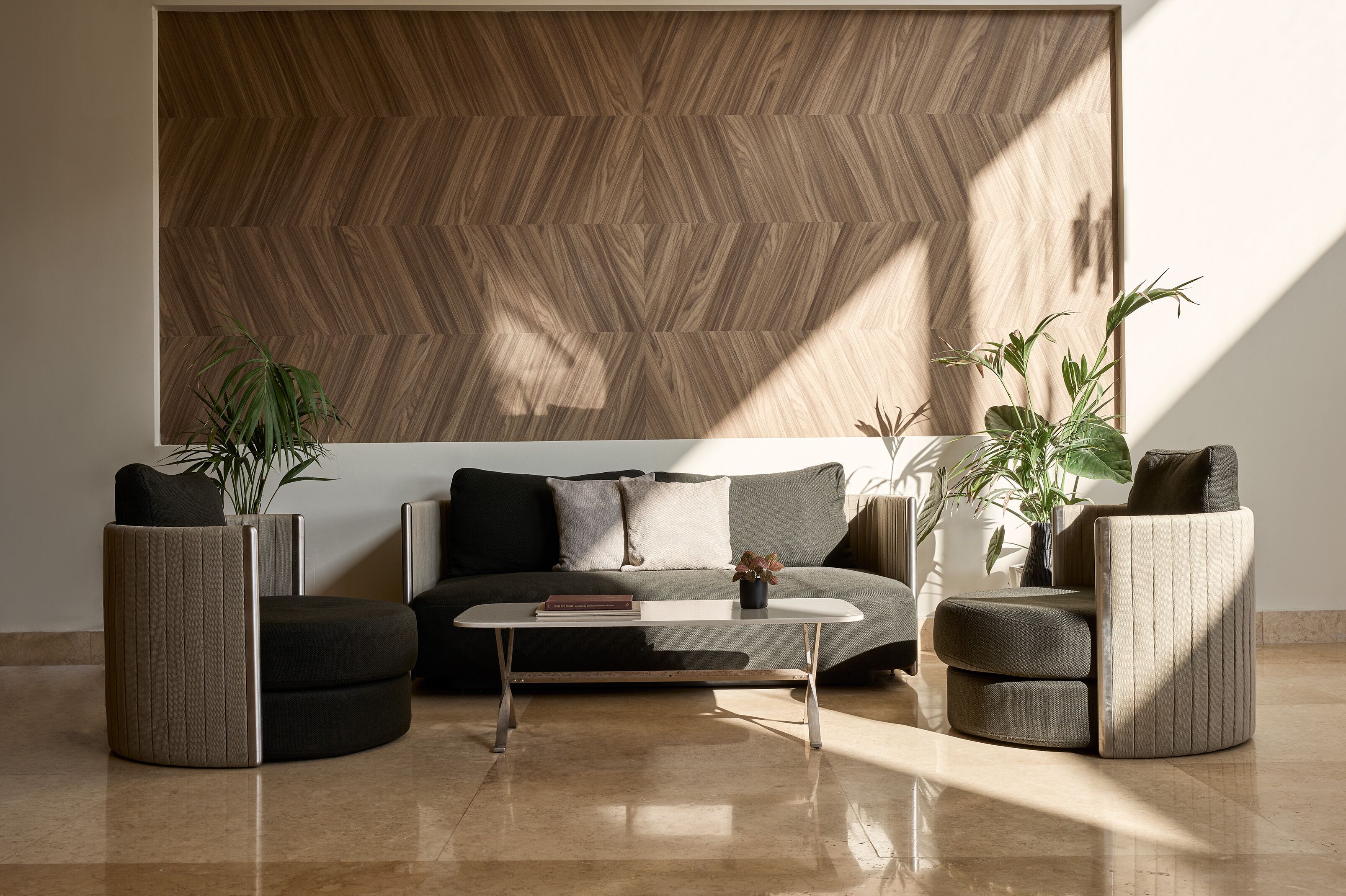 A modern living room with a sofa, two armchairs, a coffee table, and potted plants.