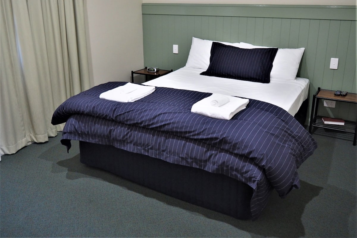 A hotel room with a bed, a nightstand, a lamp, and a window with curtains.