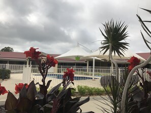 A pool area with a white fence, red flowers, and a building with a red roof in the background.