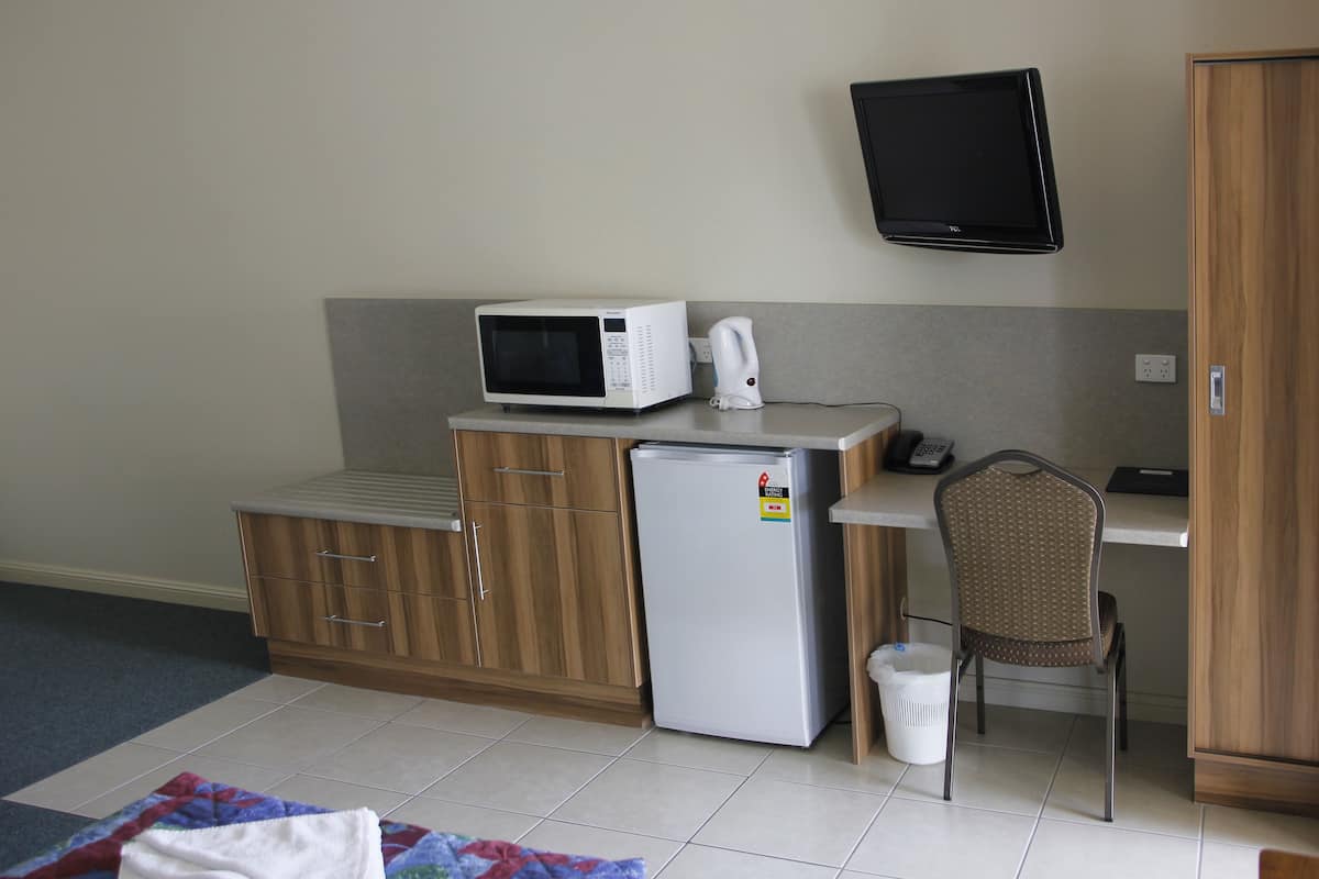 A compact kitchenette with a microwave, refrigerator, and a small chair.