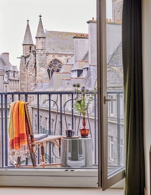 A balcony with a view of historic buildings, a chair, a small table, and a vase with flowers. - Hôtel Cartier (Saint-Malo)