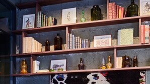 A modern room with a leather armchair, a small round table, and a bookshelf filled with books and decorative items. - Hôtel Cartier (Saint-Malo)
