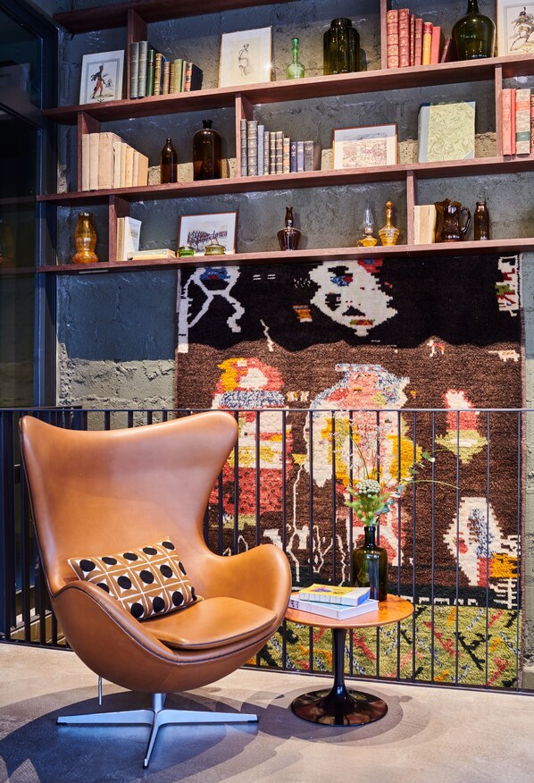 Una habitación moderna con un sillón de cuero, una mesita redonda y una estantería llena de libros y objetos decorativos.