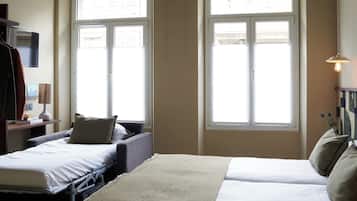 Quarto de hotel com duas camas, uma escrivaninha com abajur e janelas amplas.