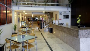Un vestíbulo de hotel con mostrador de recepción, zona de estar y una escalera que sube a un nivel superior.