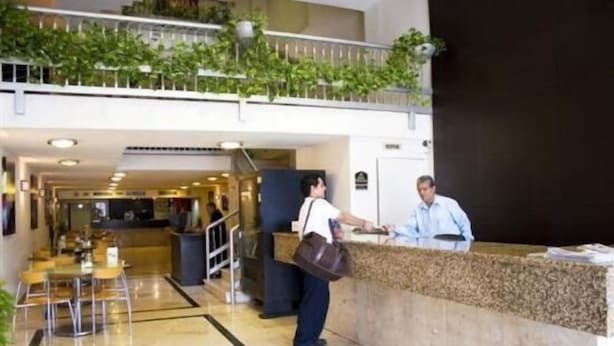 Un hall de hotel con mostrador de recepción, zona de estar y una escalera que conduce a un nivel superior.