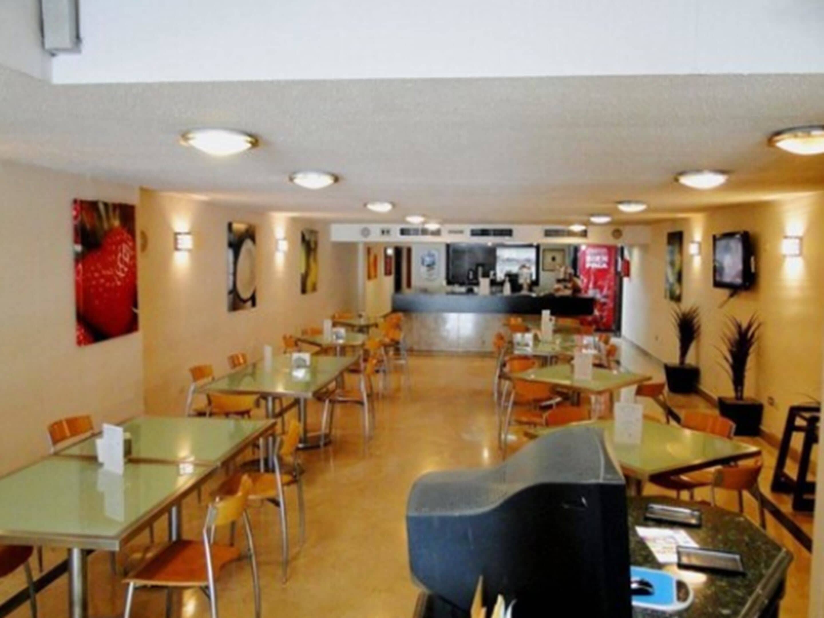 A spacious indoor dining area with multiple tables and chairs, a counter with a menu, and a television mounted on the wall.