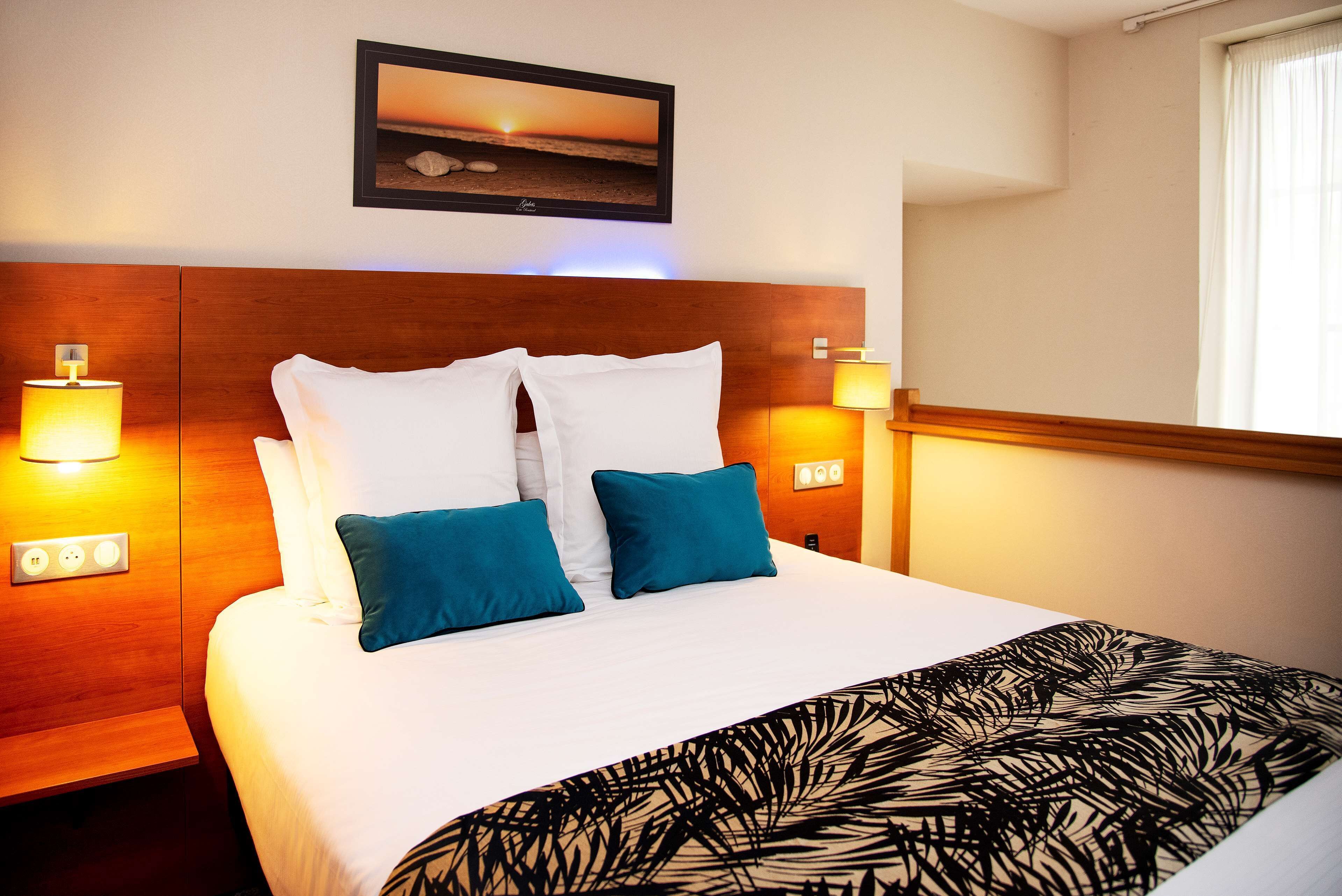 A hotel room with a large bed, two bedside lamps, a framed picture on the wall, and a window with curtains.