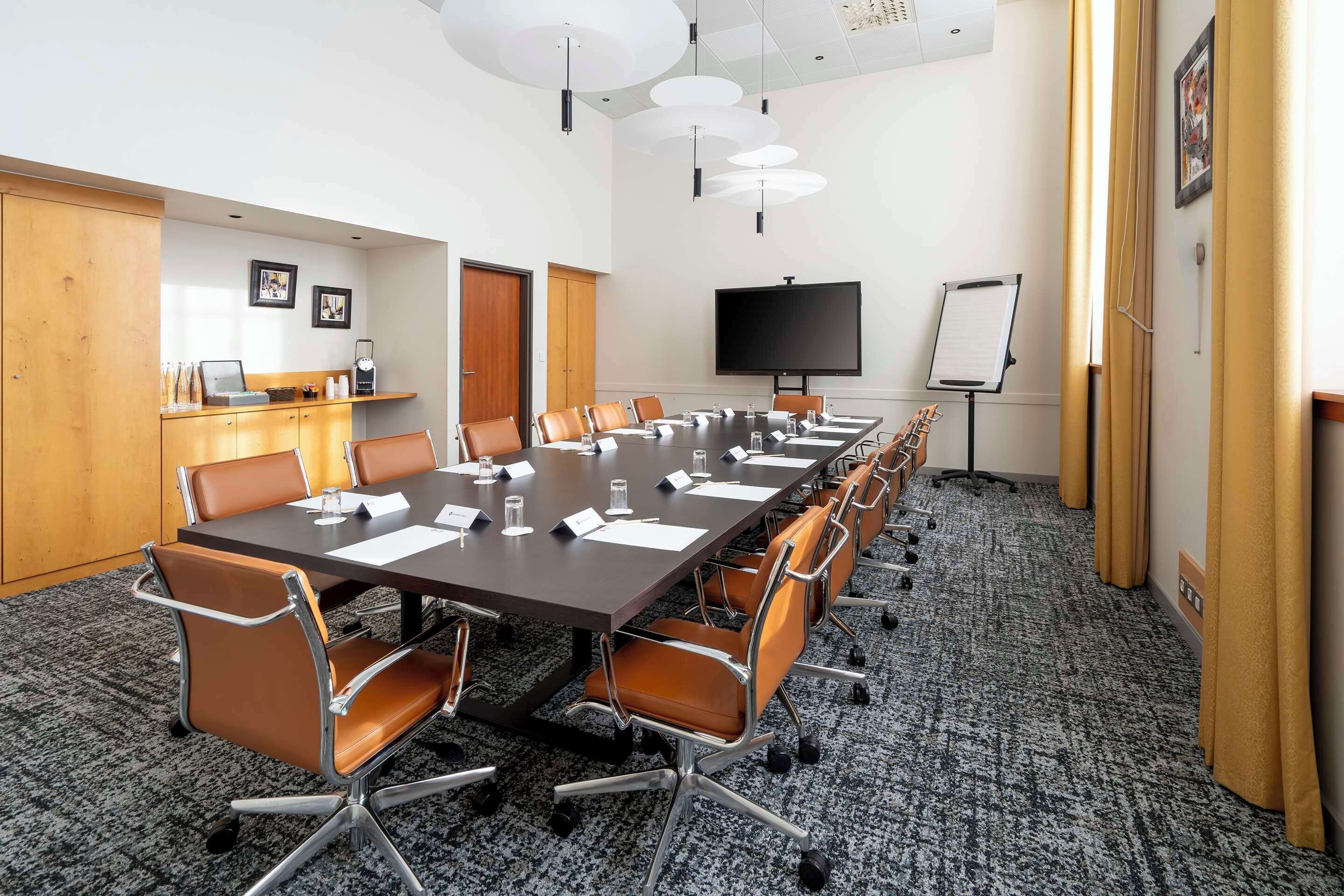 A conference room with a long table, multiple chairs, a whiteboard, and a television.