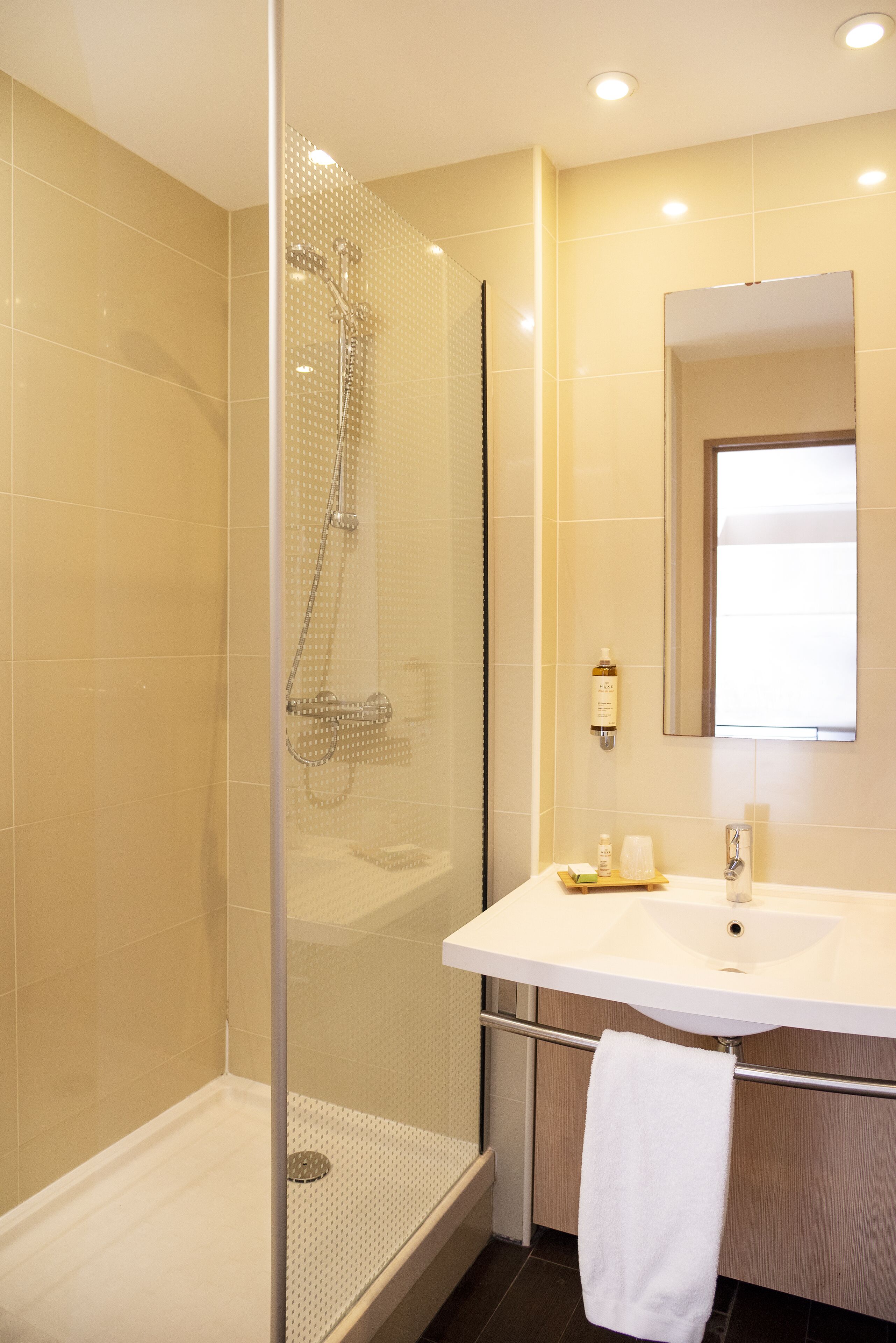 Un baño moderno con ducha envuelta en vidrio, un lavabo blanco y un espejo grande.