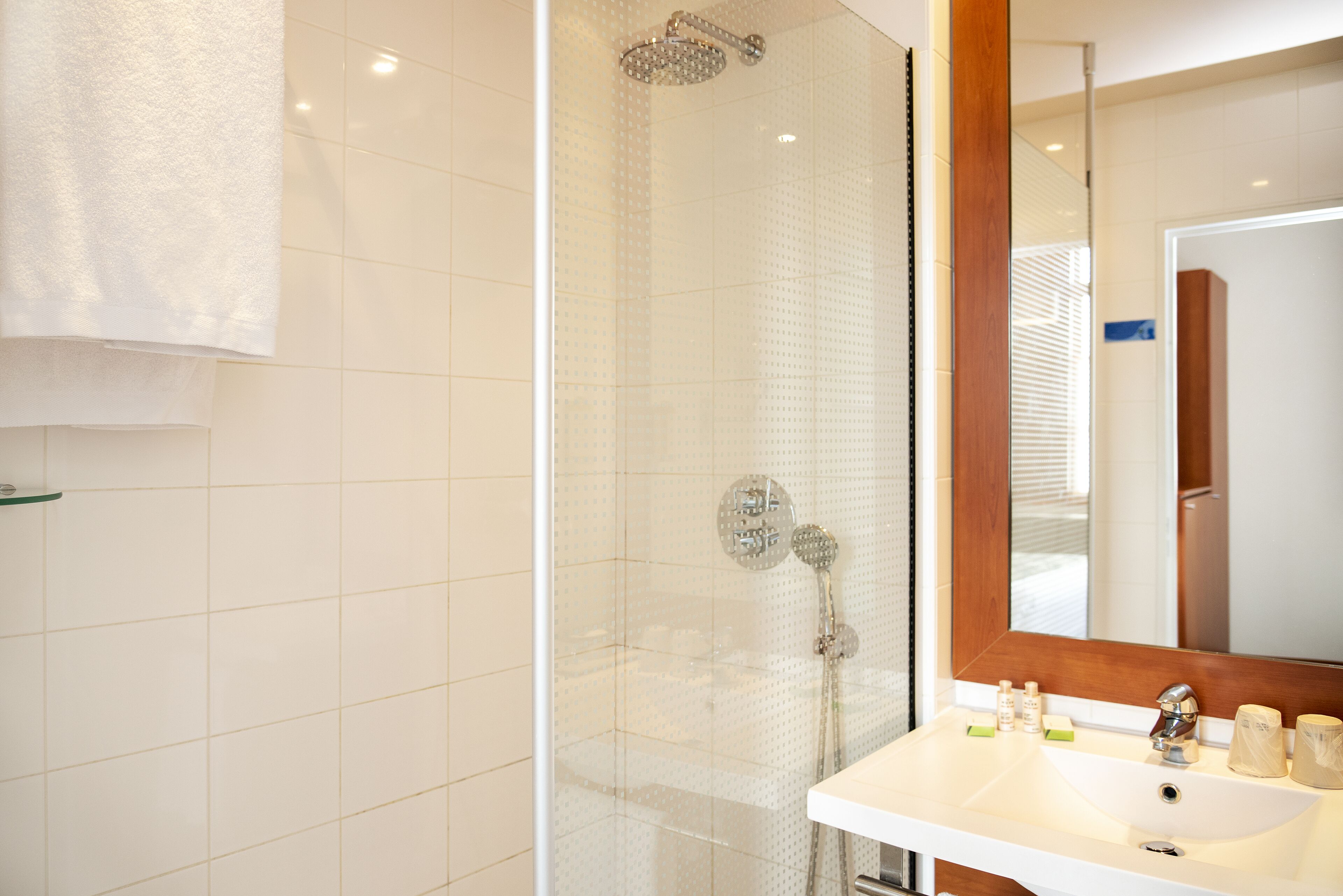 A bathroom with a glass-enclosed shower, a white sink with toiletries, and a mirror with a wooden frame.