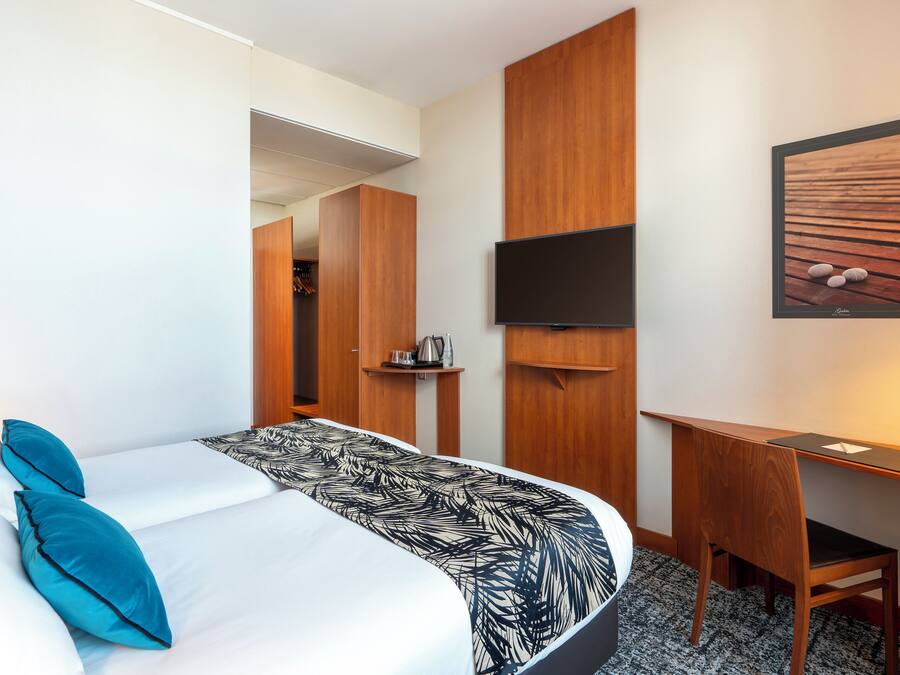 A hotel room with a bed, a desk, a chair, a television, and a framed picture on the wall.