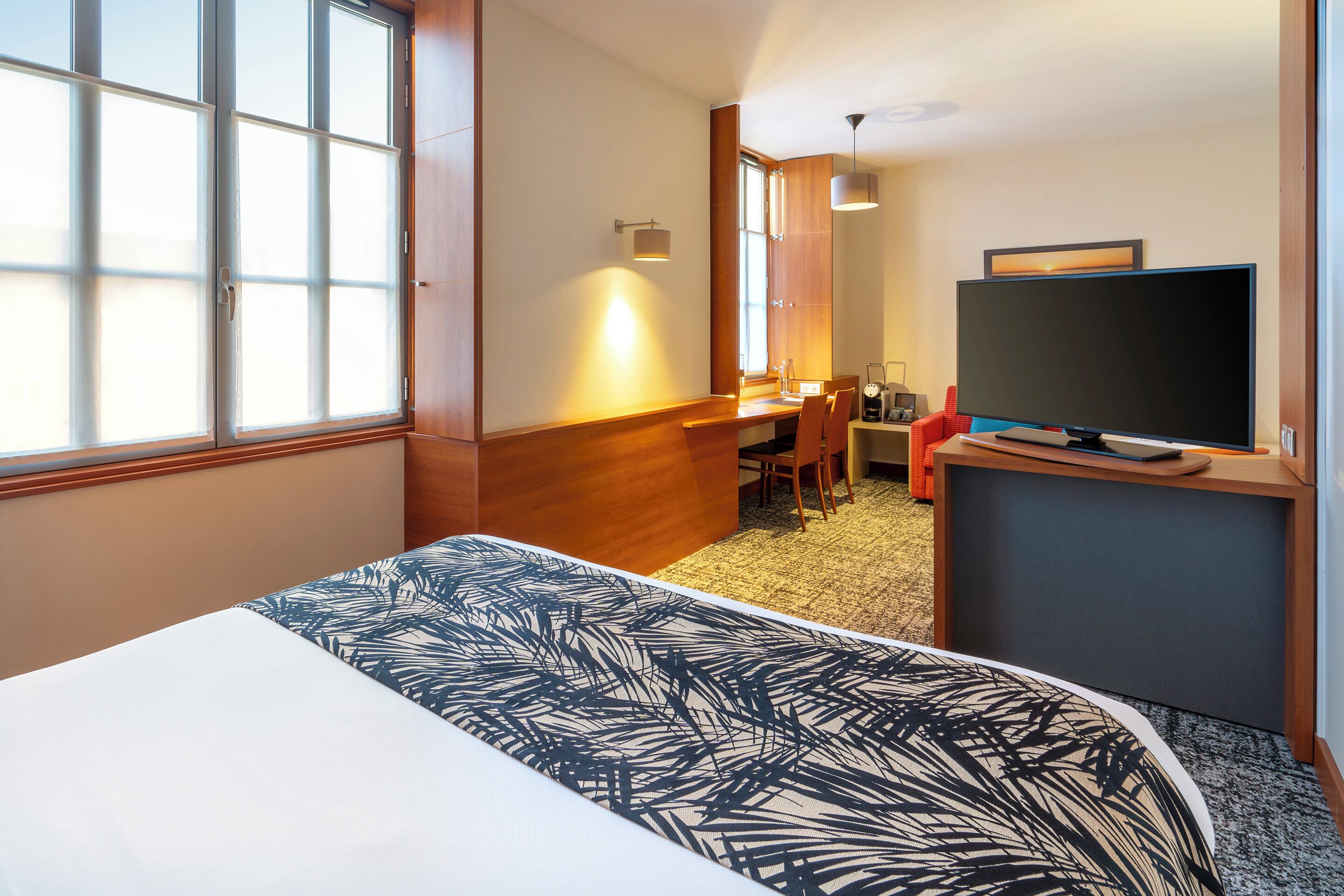 Una habitación de hotel con una cama grande, un escritorio con silla, un televisor y una ventana con persianas.