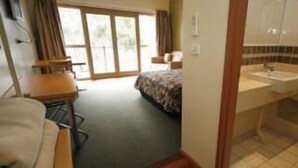 A hotel room with a bed, a desk, a chair, a bathroom with a sink and shower, and a large window. - Forbes Victoria Inn (Forbes)