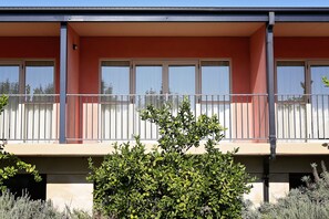 Un edificio a due piani con un balcone, ampie finestre e un piccolo giardino.