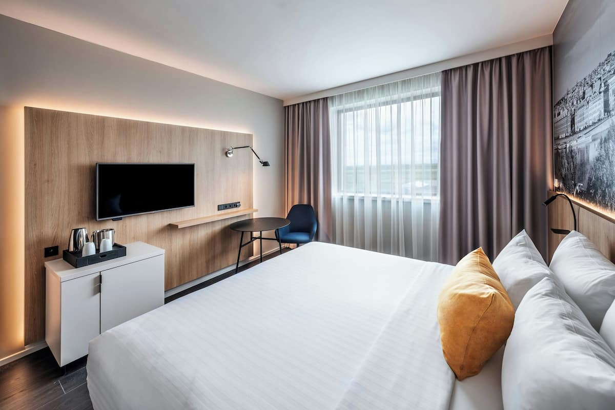 Een moderne hotelkamer met een groot bed, een bureau met een flatscreen-televisie, een stoel en een raam met gordijnen.