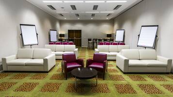 A conference room with white sofas, a central round table, and two large screens on stands.