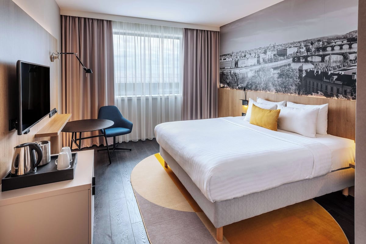 Een hotelkamer met een bed, een bureau met een televisie, een stoel, een raam met gordijnen en een stadsgezicht op de muur.