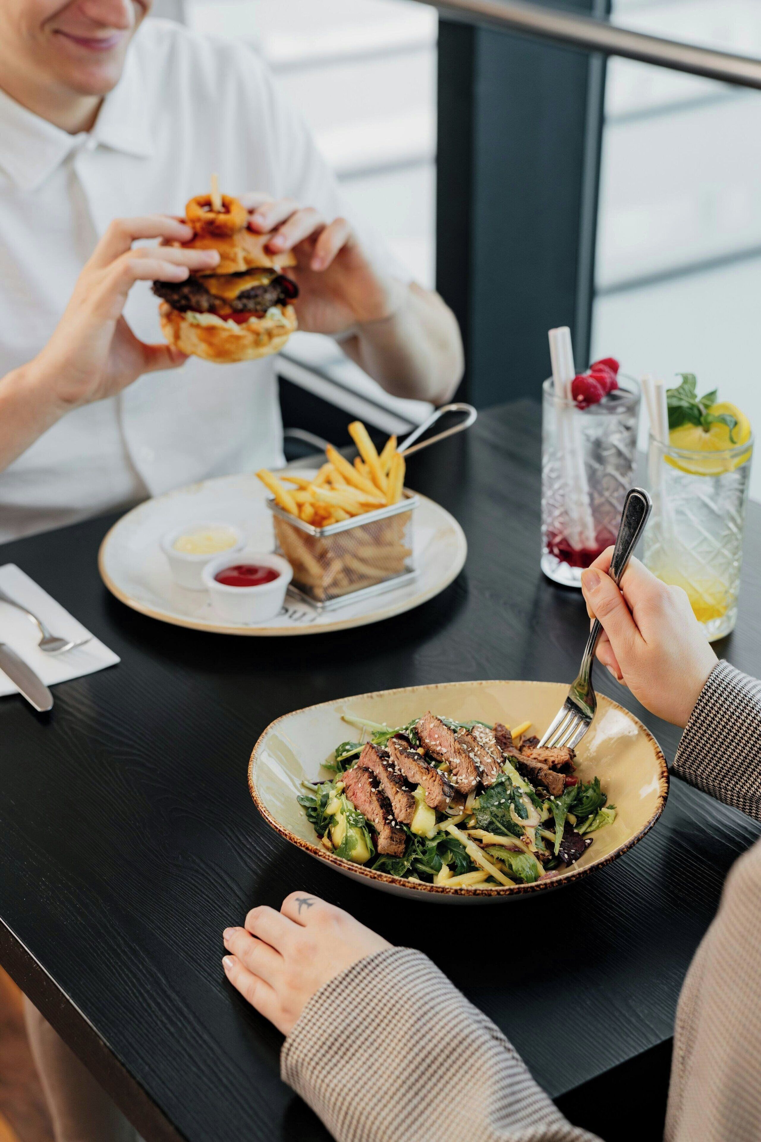 A dining table with a meal consisting of a burger, fries, and a salad.