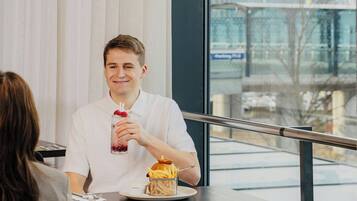 A person sitting at a table with a meal, a window with a view of a building, and a railing.
